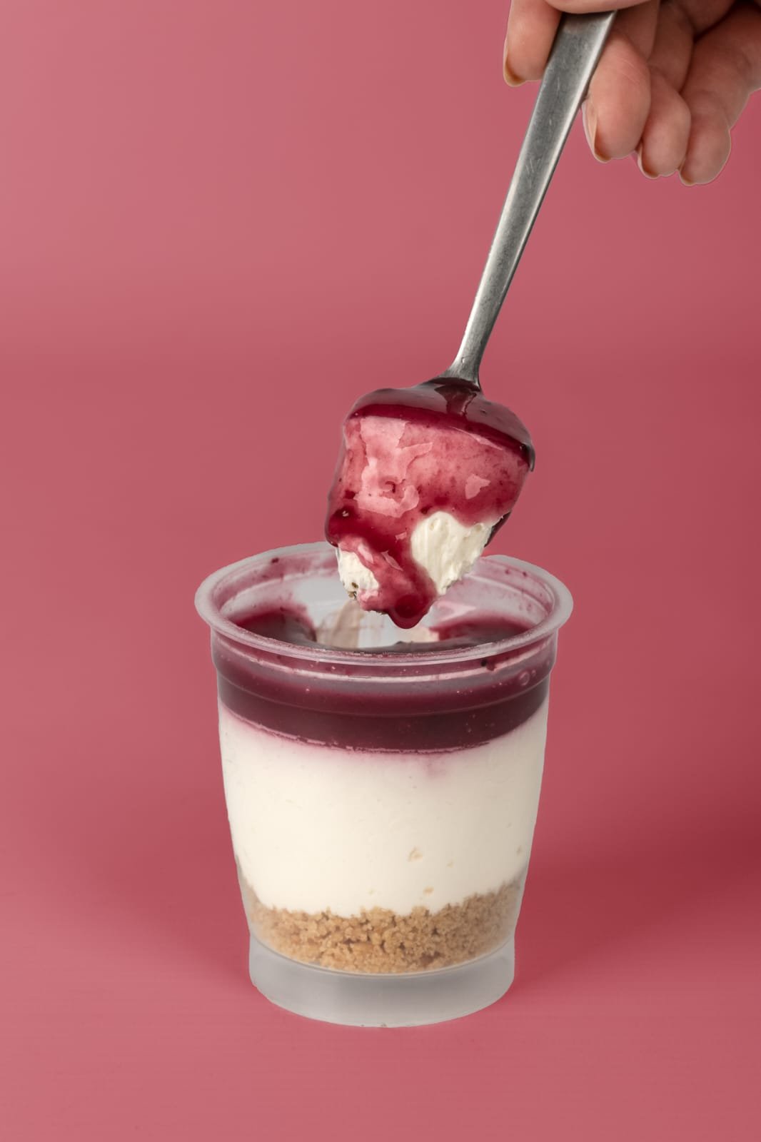 Una cucharada de cheesecake con cobertura de frutos rojos, sobre un fondo rosa.