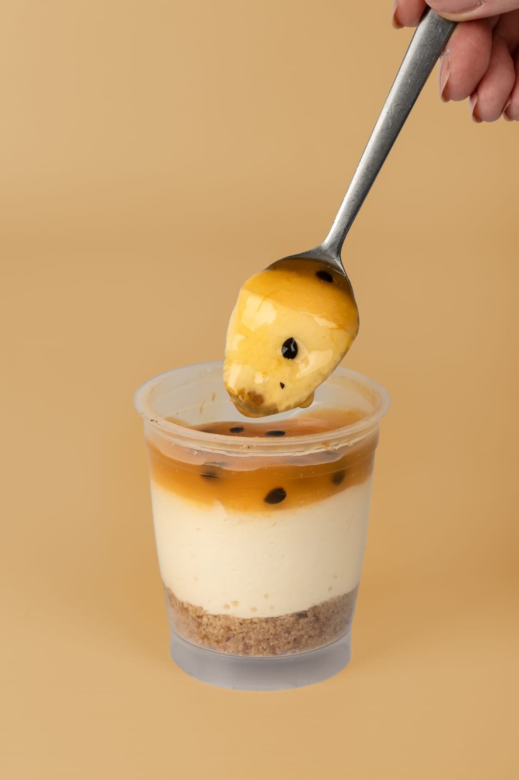Cheesecake de maracuyá con una cucharada de su cobertura, sobre un fondo dorado.